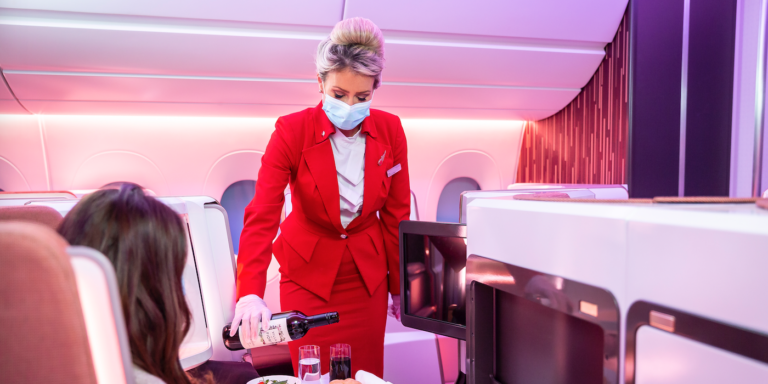 a stewardess in a virgin upper class cabin pouring wine for a guest