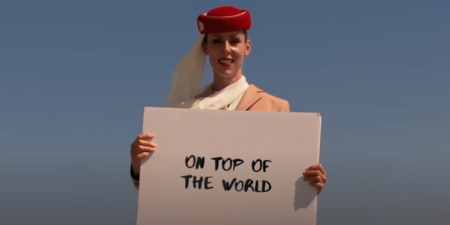 an emirates female cabin crew member in full uniform delivering a message on the tip of the Burj Khalifa by Emaar in dubai