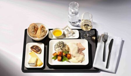 A black airline meal tray with white plates featuring luxury foods