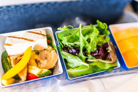 Healthy vegan hot food vgml snack meal on airplane flight with grilled tofu, vegetables, fruit and green fresh salad macro closeup