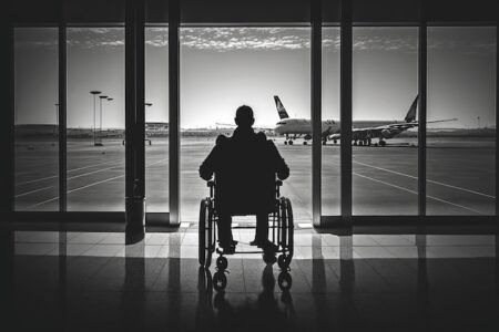 man in wheelchair, waiting for flight departure, with view of the tarmac and planes, created with generative ai