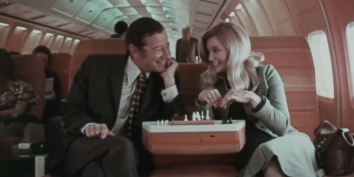 A male and female passenger on a Braniff Boeing 727 flight playing a game of chess using a table created by the folded down seatback of the centre economy class seat