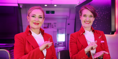 Two female Virgin Atlantic crew members welcoming guests on board an aircraft using sign language