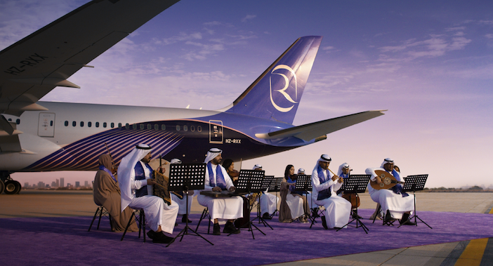 An orchestra playing instruments in front of a Riyadh Air aircraft on a runway