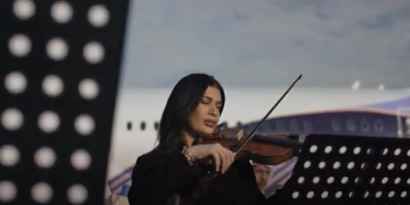 A female playing the violin in front of an airplane