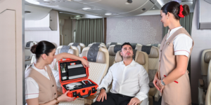 Two female Emirates cabin crew attending to a male passenger, using a medical kit in an orange case