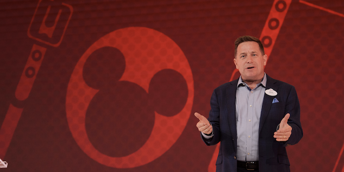Jeff James speaking on stage at a Disney Institute event, with a Mickey Mouse graphic on the wall behind