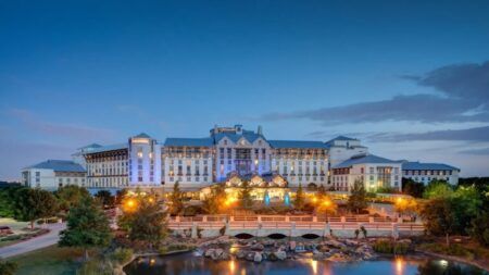 Large white resort hotel with Texas-style architecture illuminated at twilight, featuring landscaped grounds with pond and fountain in foreground