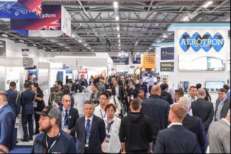 Farnborough Airshow 2026 expands with sixth hall amid record exhibitor demand A crowded exhibition hall at Farnborough Airshow with business professionals networking among aerospace company booths including Aerotron Composites