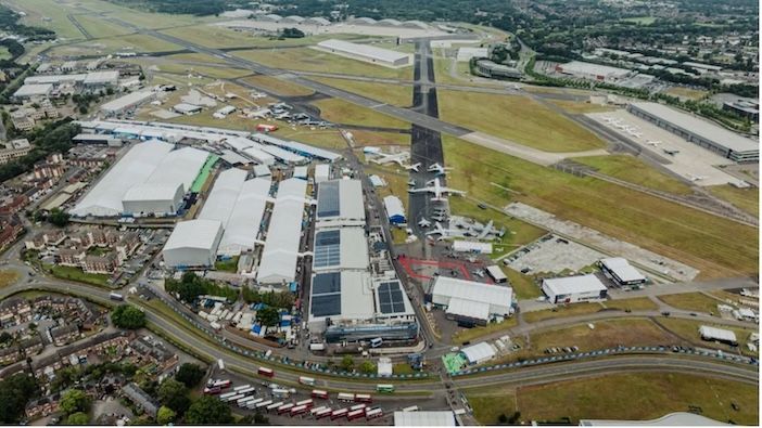 An aerial view of Farnborough International Airshow exhibition halls showing multiple white tent-like structures with parked aircraft visible on the tarmac