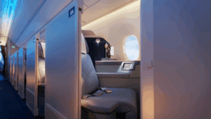 PAL's A350-1000 business class seat with privacy partition, showing aisle access, personal window, and modern gray upholstery in cabin with blue ambient lighting"