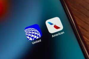A close-up of an iPhone screen displaying the United Airlines and American Airlines app icons side by side, against a blurred colorful background.