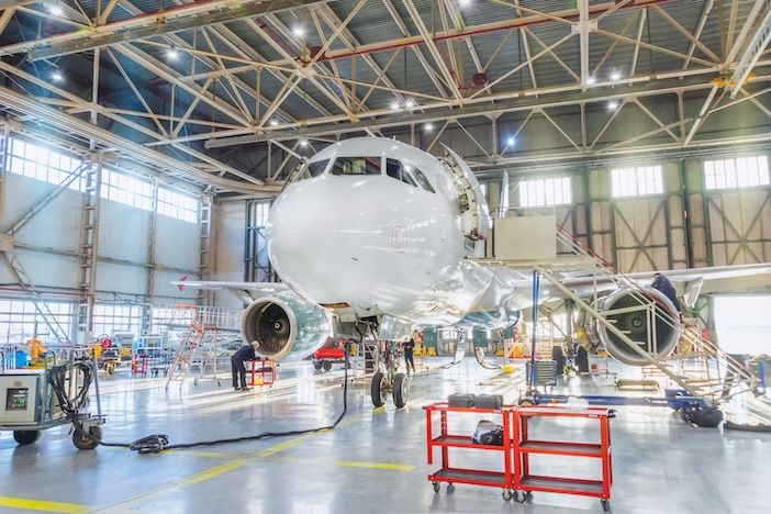 Aircraft inside the aviation hangar, maintenance service. Airplane technician worker working around. Bright light outside the gate