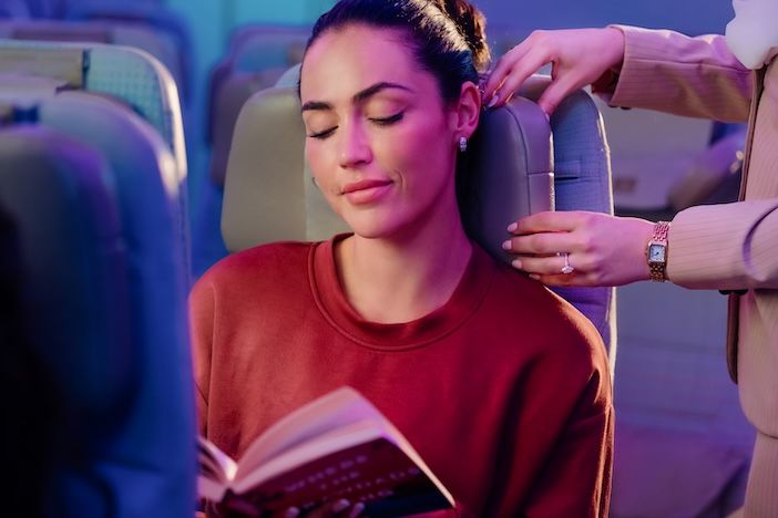 A female passenger relaxing in an Emirates Economy Class seat while using the U-Dream headrest