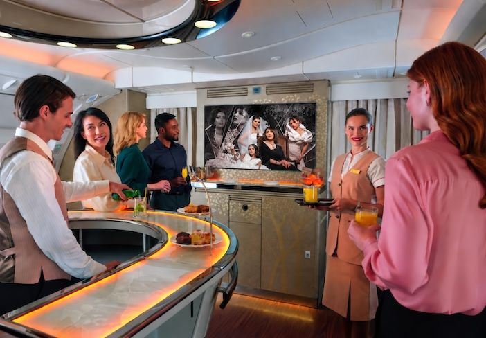 The image shows Emirates passengers enjoying Dubai+ at the first and business class onboard lounge - a dedicated selection of Emirati and regional entertainment available through the airline’s award-winning ice inflight entertainment system